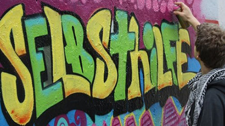 Junger Mann gestaltet Wort Selbsthilfe als Graffiti